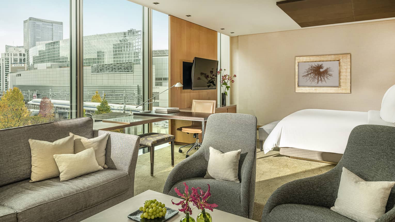 Junior suite with gray sofa, armchairs, work desk by a window with plaza view and king bed in the background