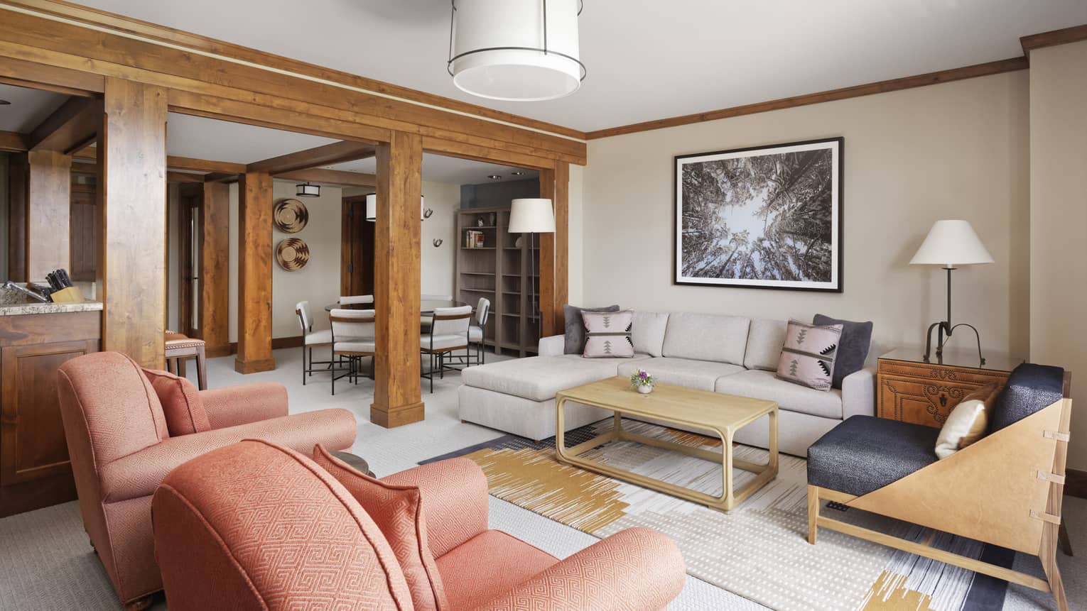 Living room with a sofa, two arm chairs and wooden beams separating dining area