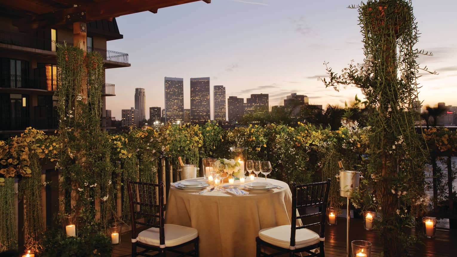 Round candle-lit dining table with wine, glasses in garden patio corner