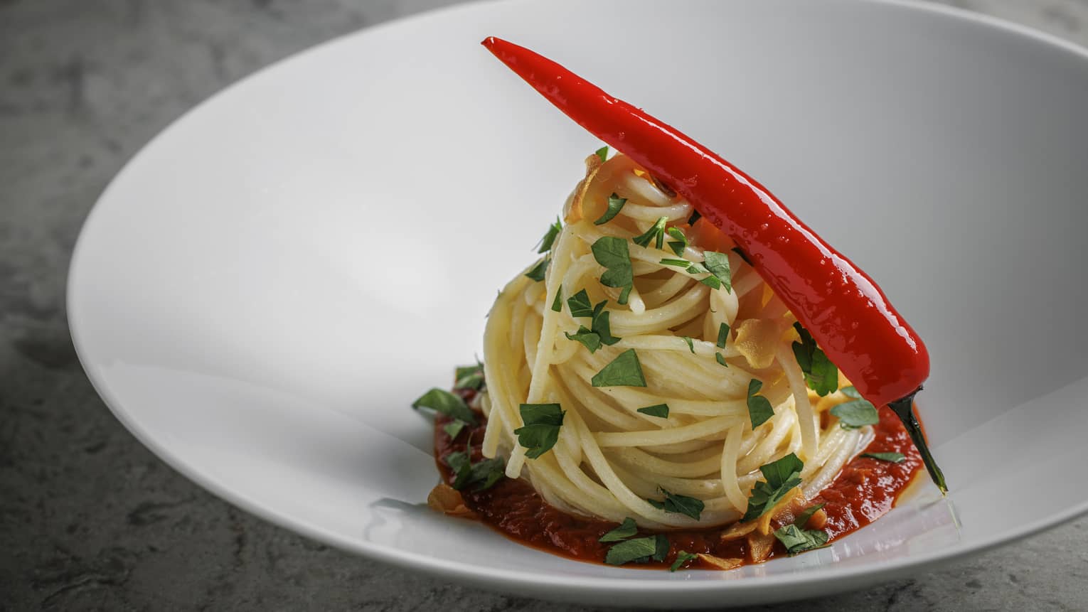 Twirled spaghetti dish in shallow white bowl topped with whole fresh chilli