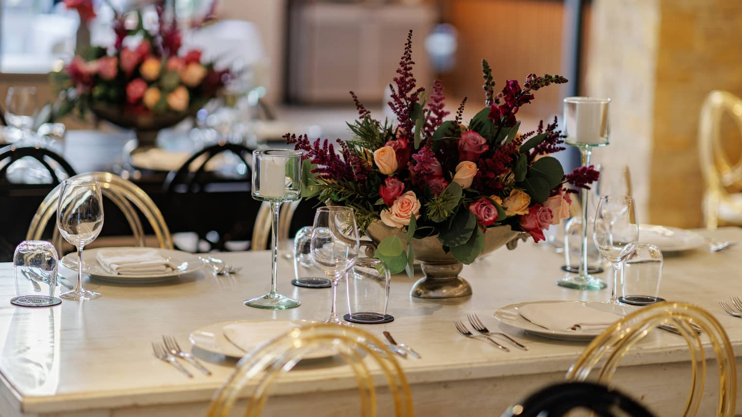 Close up of floral table centrepiece comprised of burgundy, peach and green in the middle of a white table