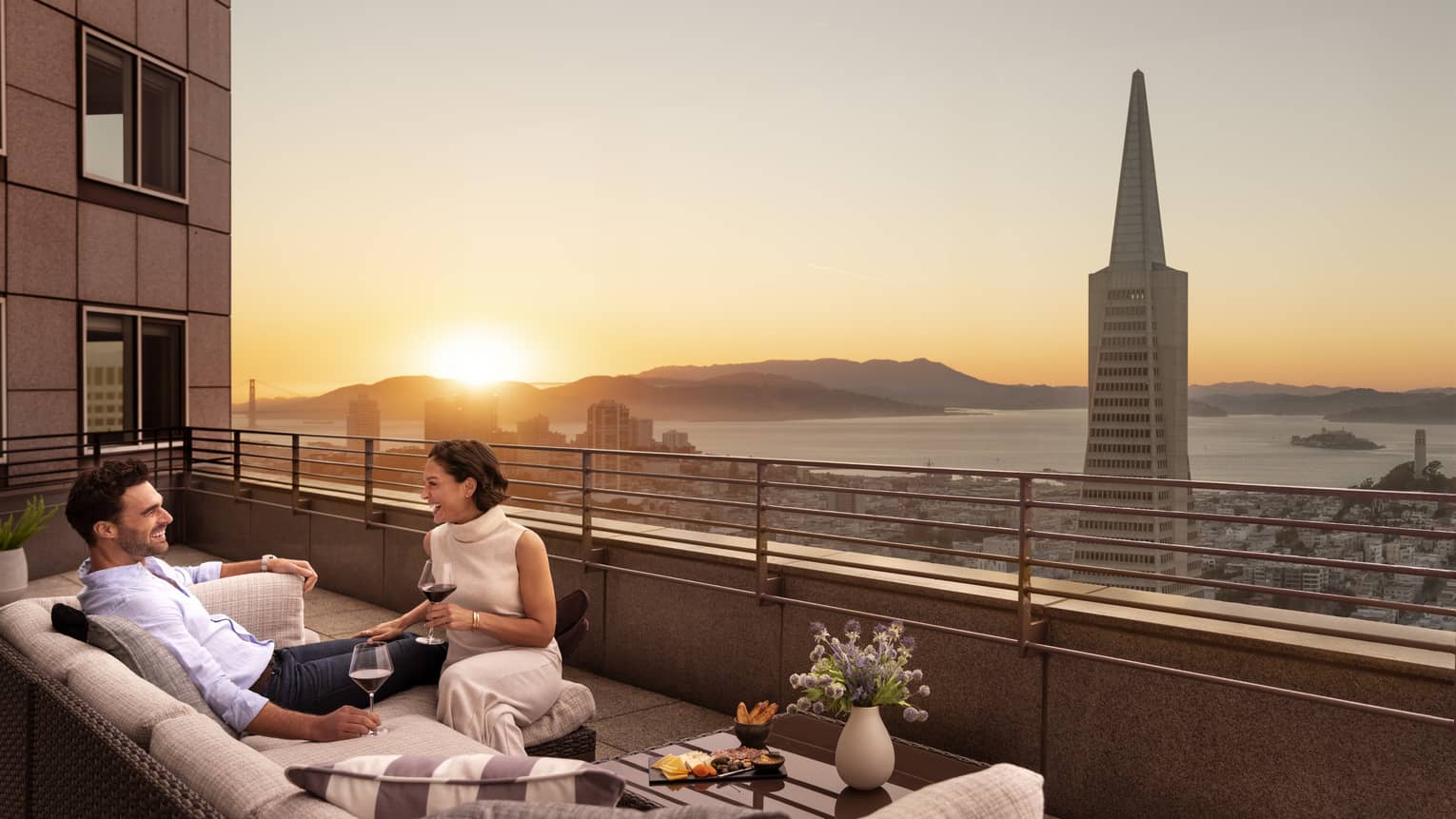 A couple laughs together on their private terrace overlooking San Francisco at Four Seasons Hotel San Francisco at Embarcadero.