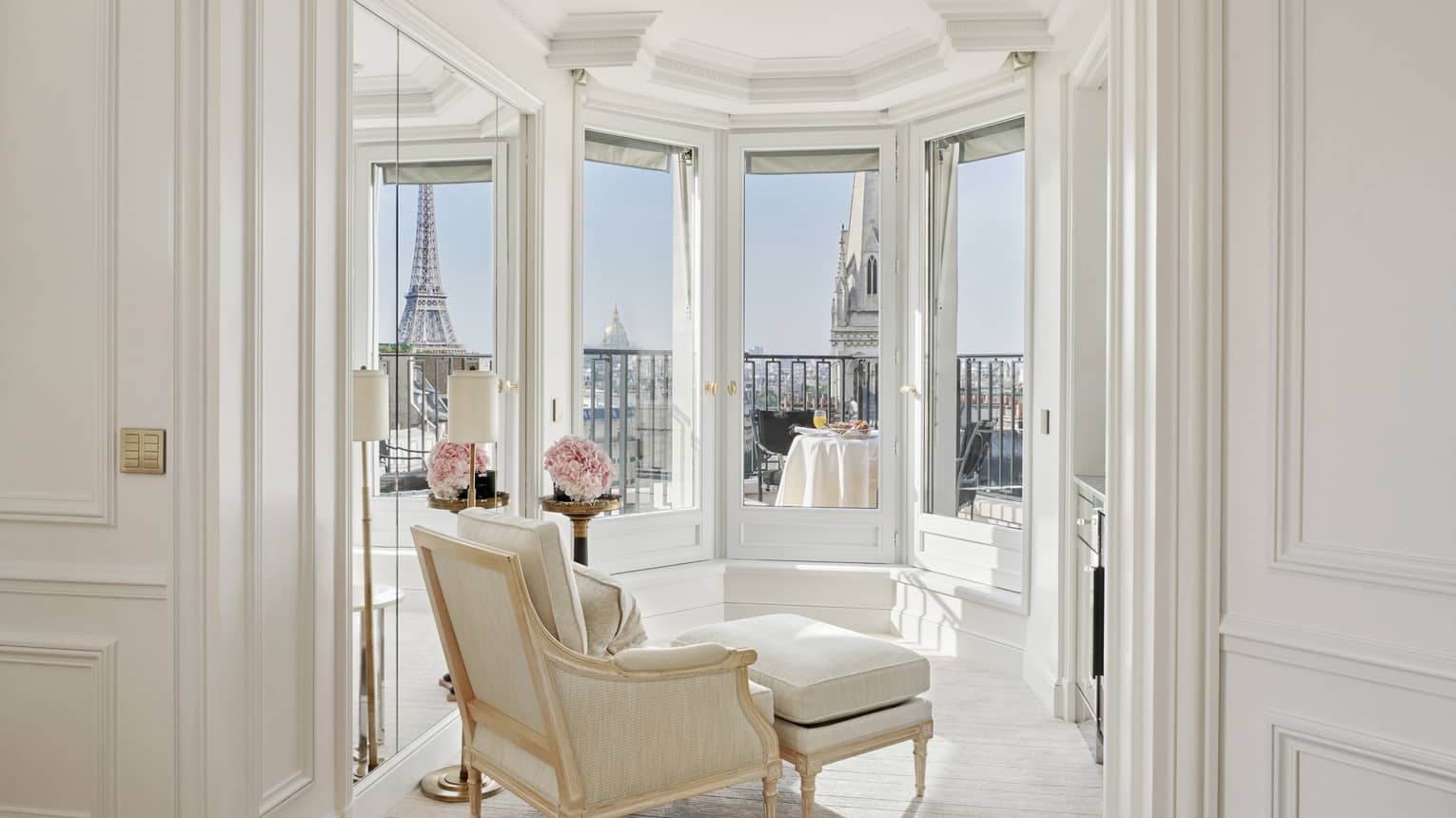A white room has windows and a balcony with a direct view of the Eiffel Tower