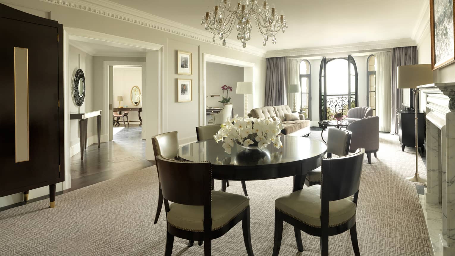 One-bedroom Suite round dining room table for 6, small crystal chandelier, living room, French doors to balcony in background