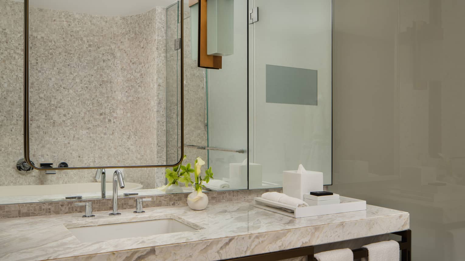 Luxury hotel bathroom vanity with marble countertop, a large mirror, a small vase with flowers, and neatly arranged toiletries
