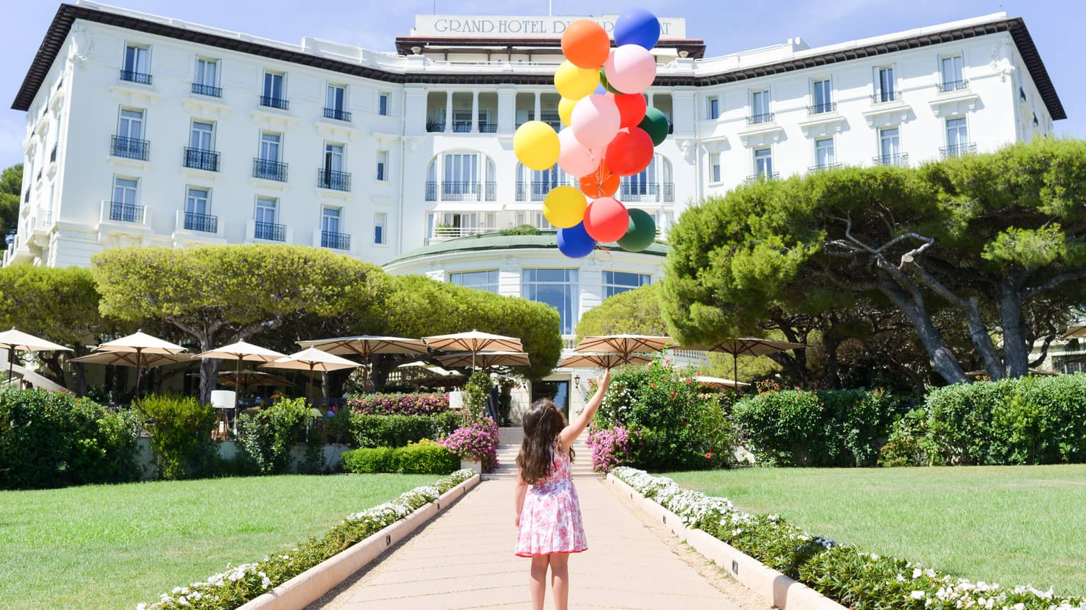 Young girl holds bunch of colourful balloons on brick path leading to hotel