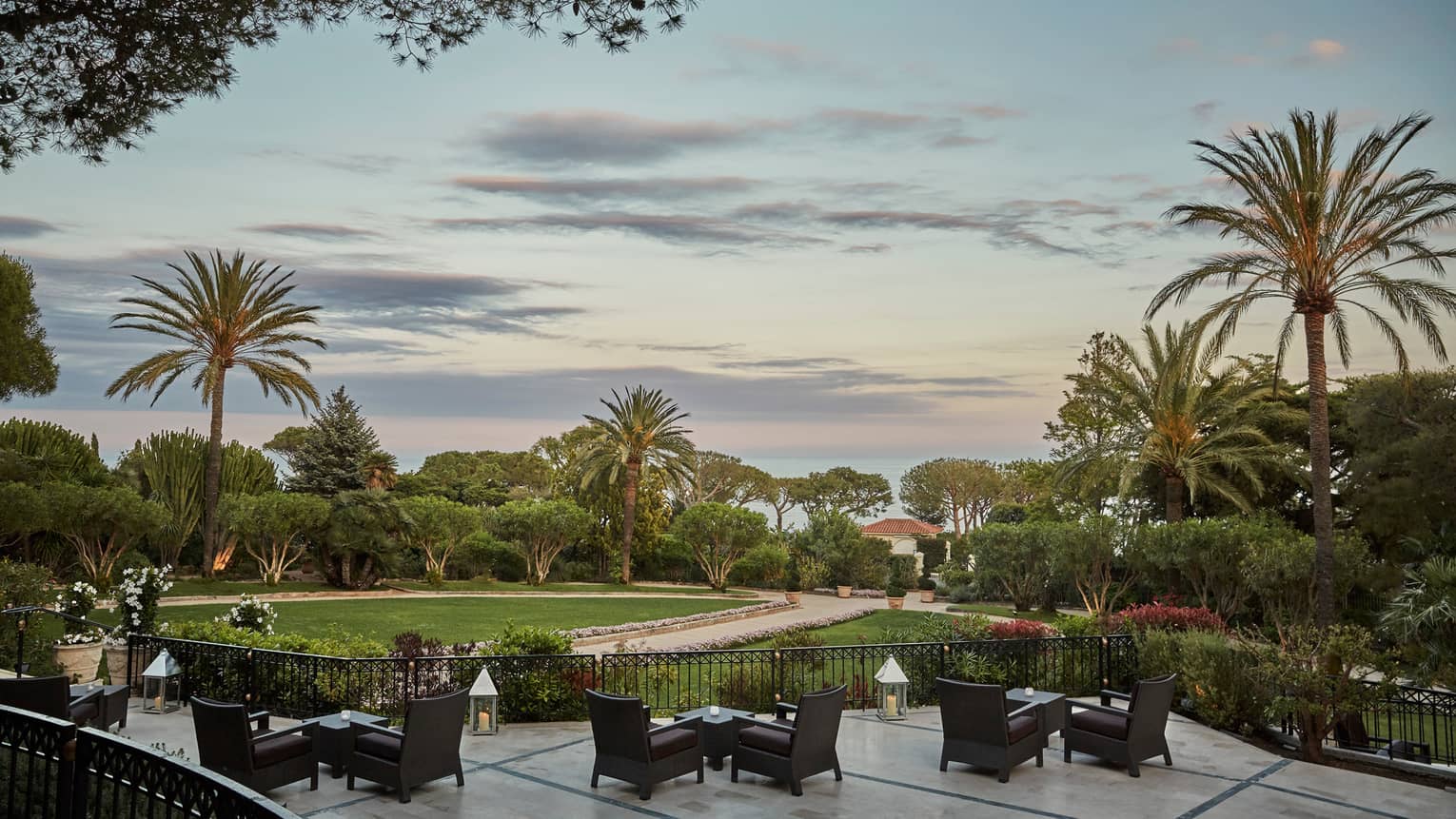 Le Bar patio dining tables, chairs by fence, gardens at sunset