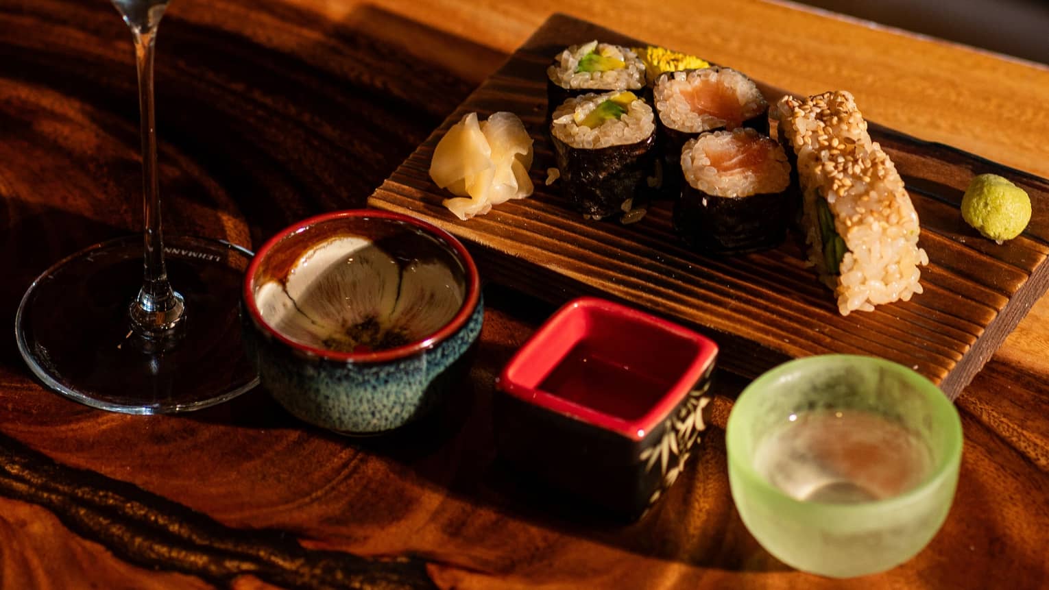 A glass of sake paired with sushi served on a wooden plate with decorate ceramic bowls