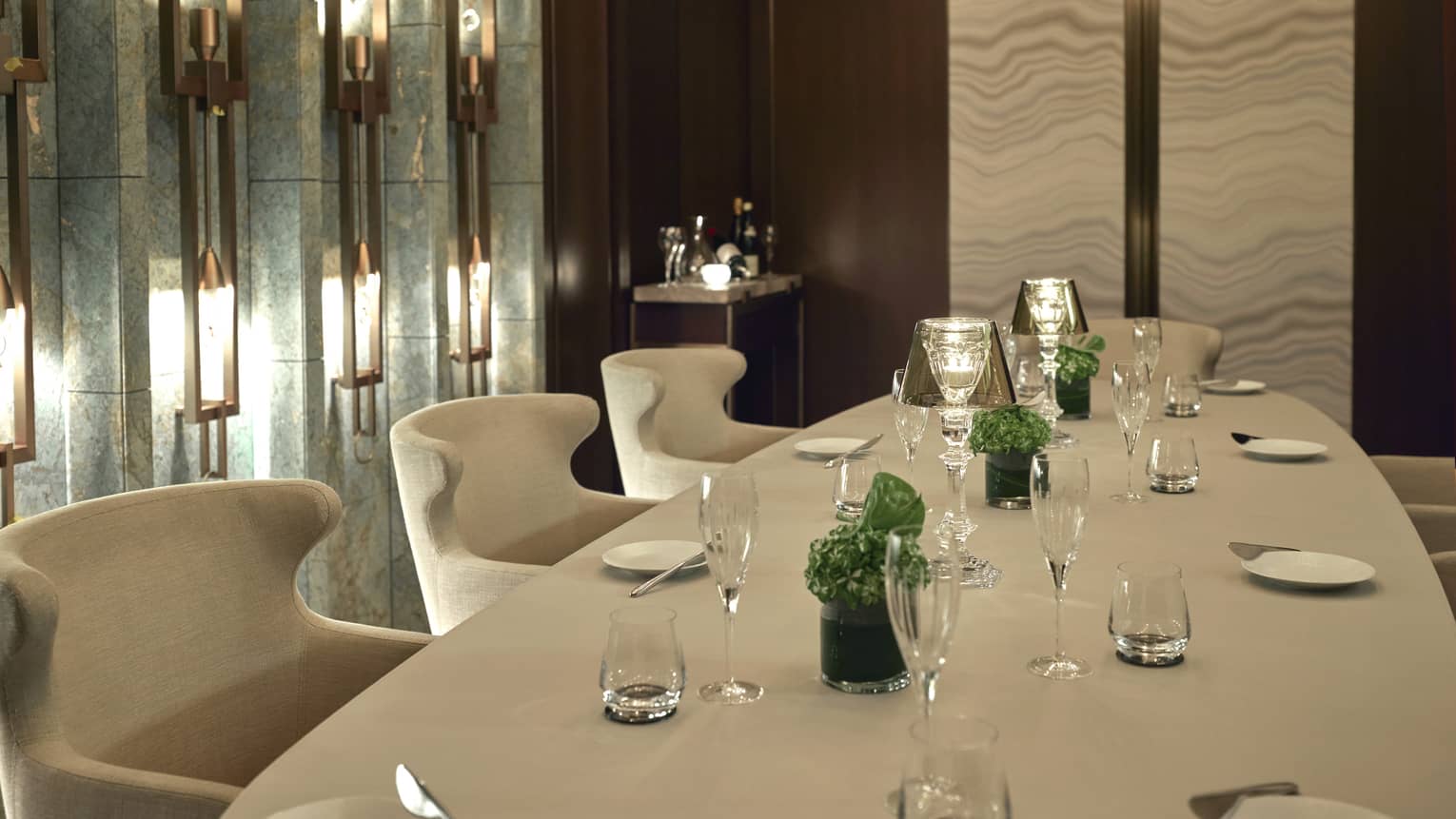 Rectangular table set for eight with white linens and minimal green centerpieces, lighted wall sconces to the left