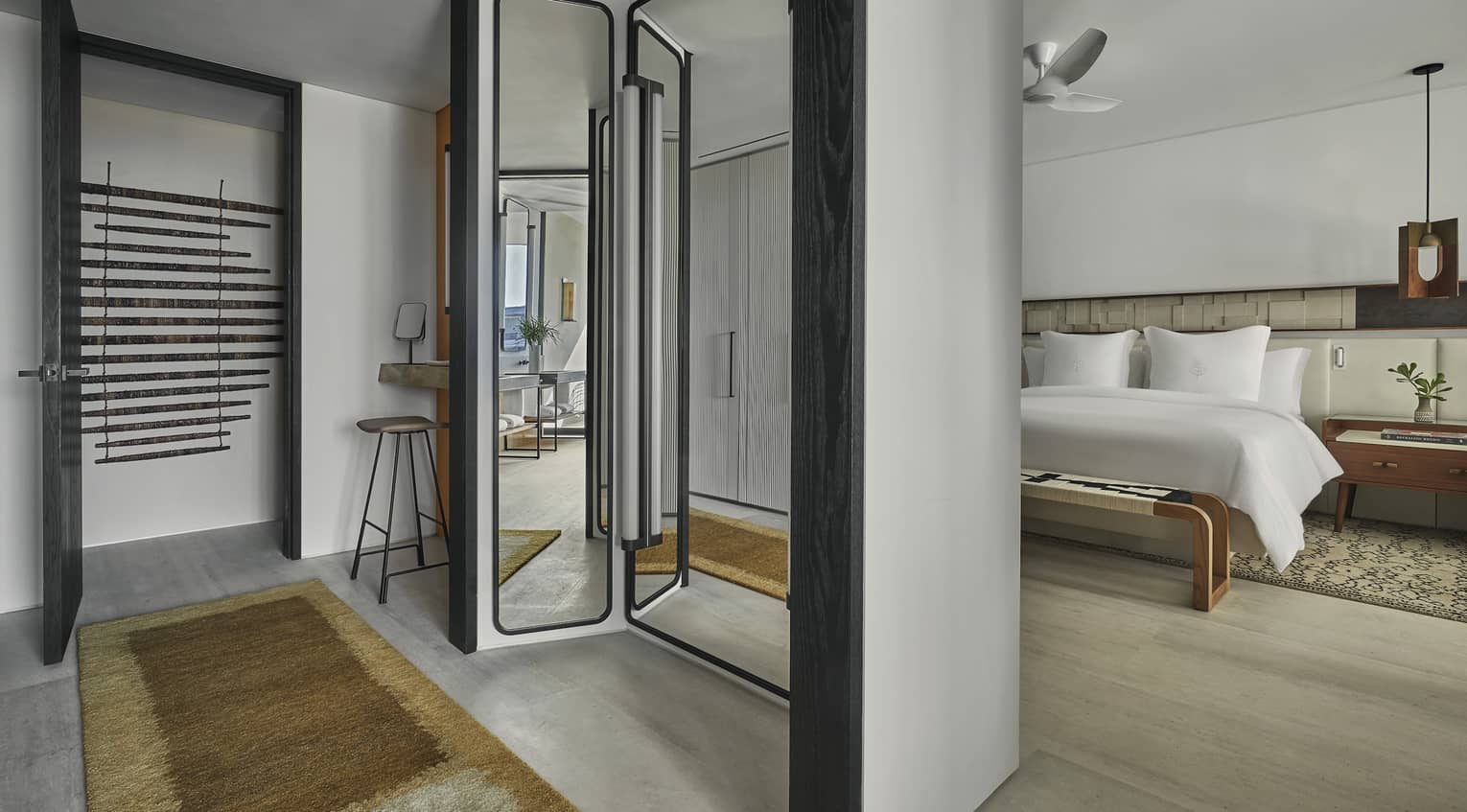 A hotel room with a bed, mirror, bench and small table.