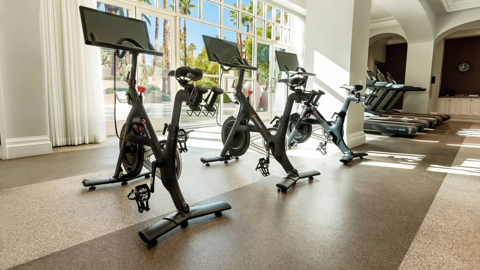 Three Peloton bikes near large windows.