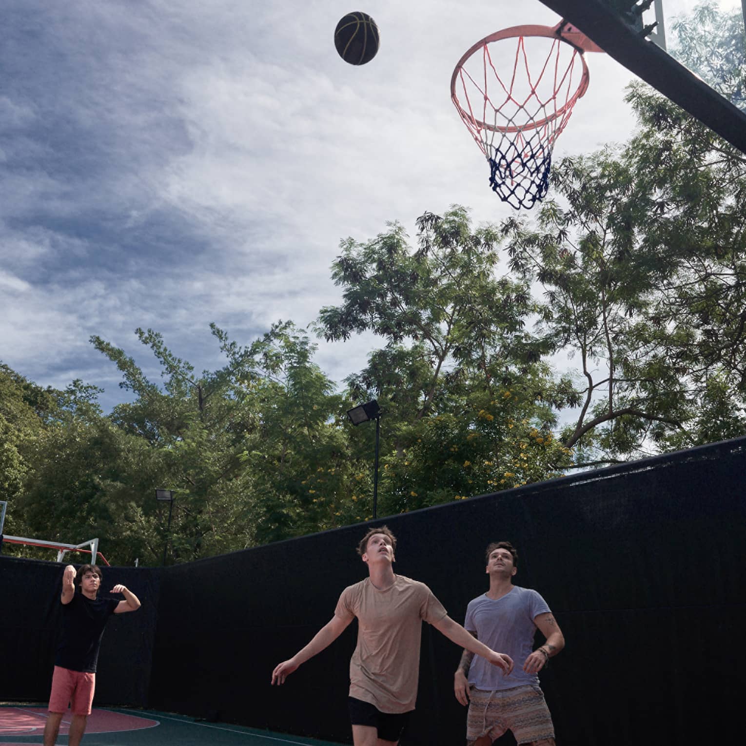 Three teenage boys play basketball on an outdoor court