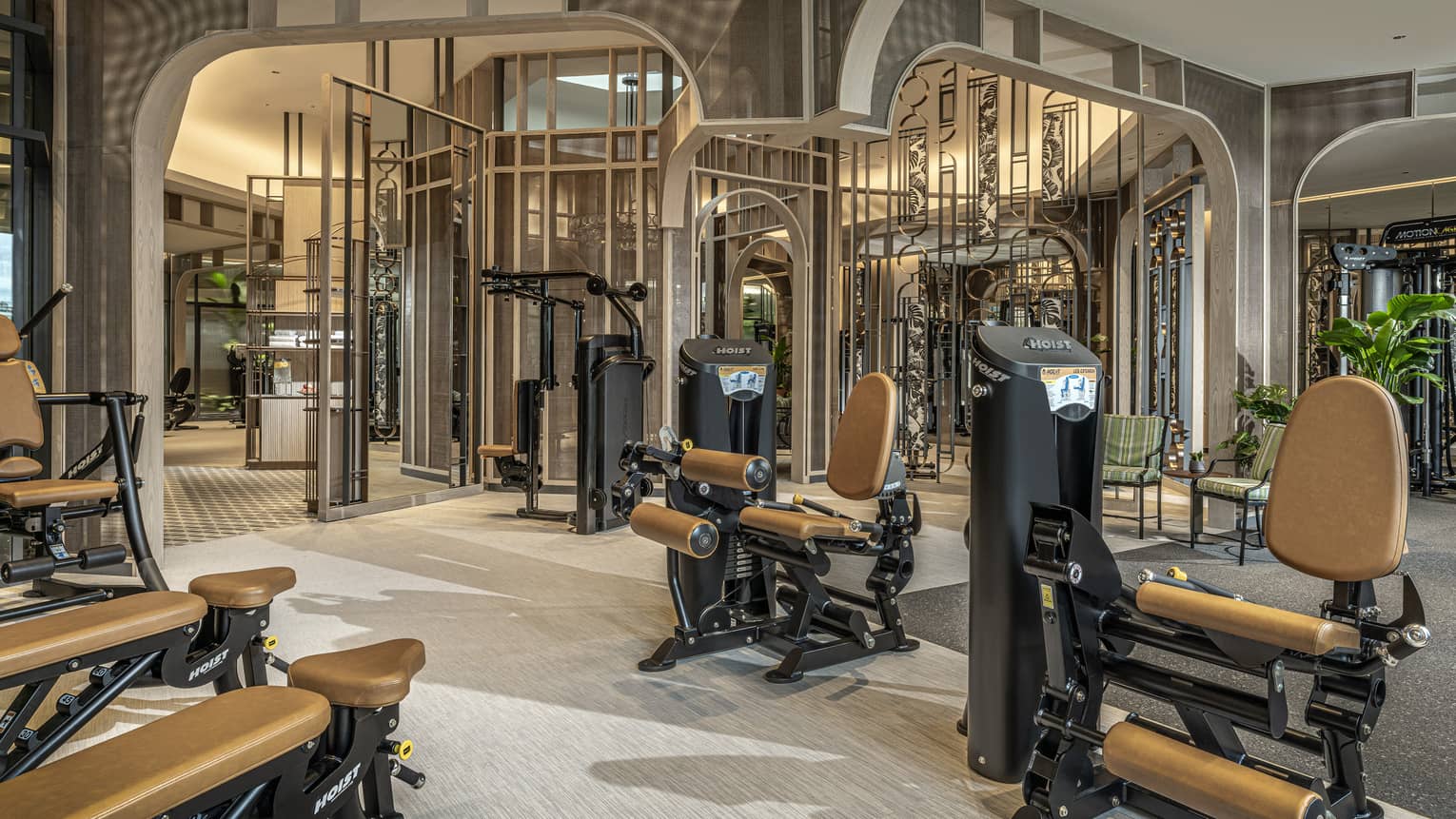 Fitness room with tan and black equipment, high ceilings, potted greenery
