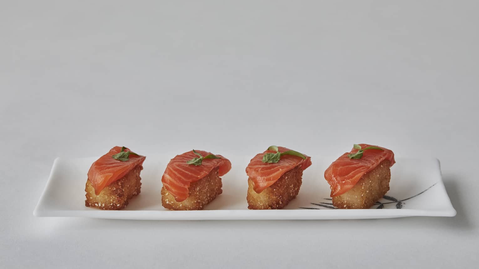 Four salmon bites on a white, rectangular porcelain plate