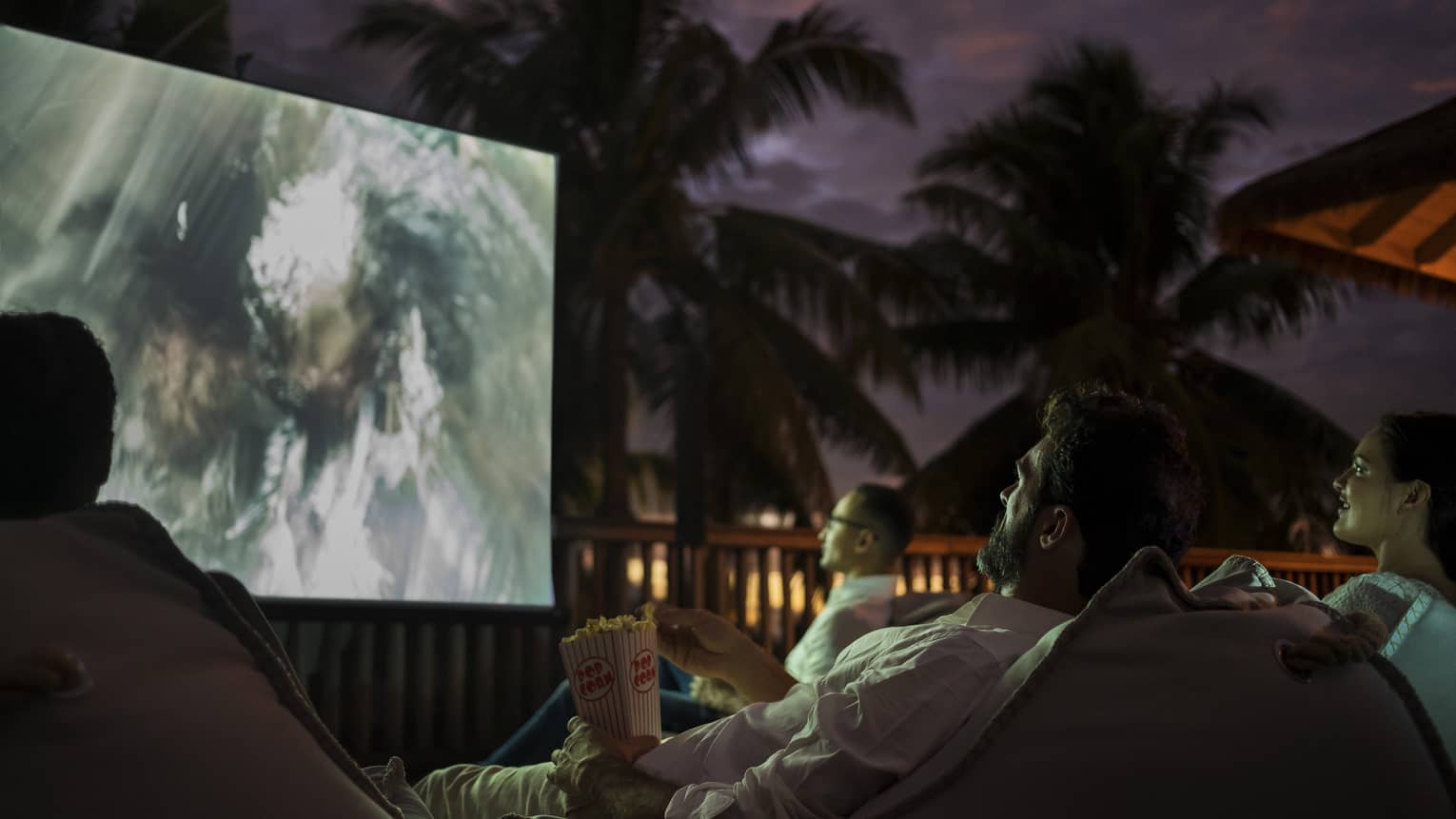 Group of people sit on bean bags with popcorn watching movie under the stars 