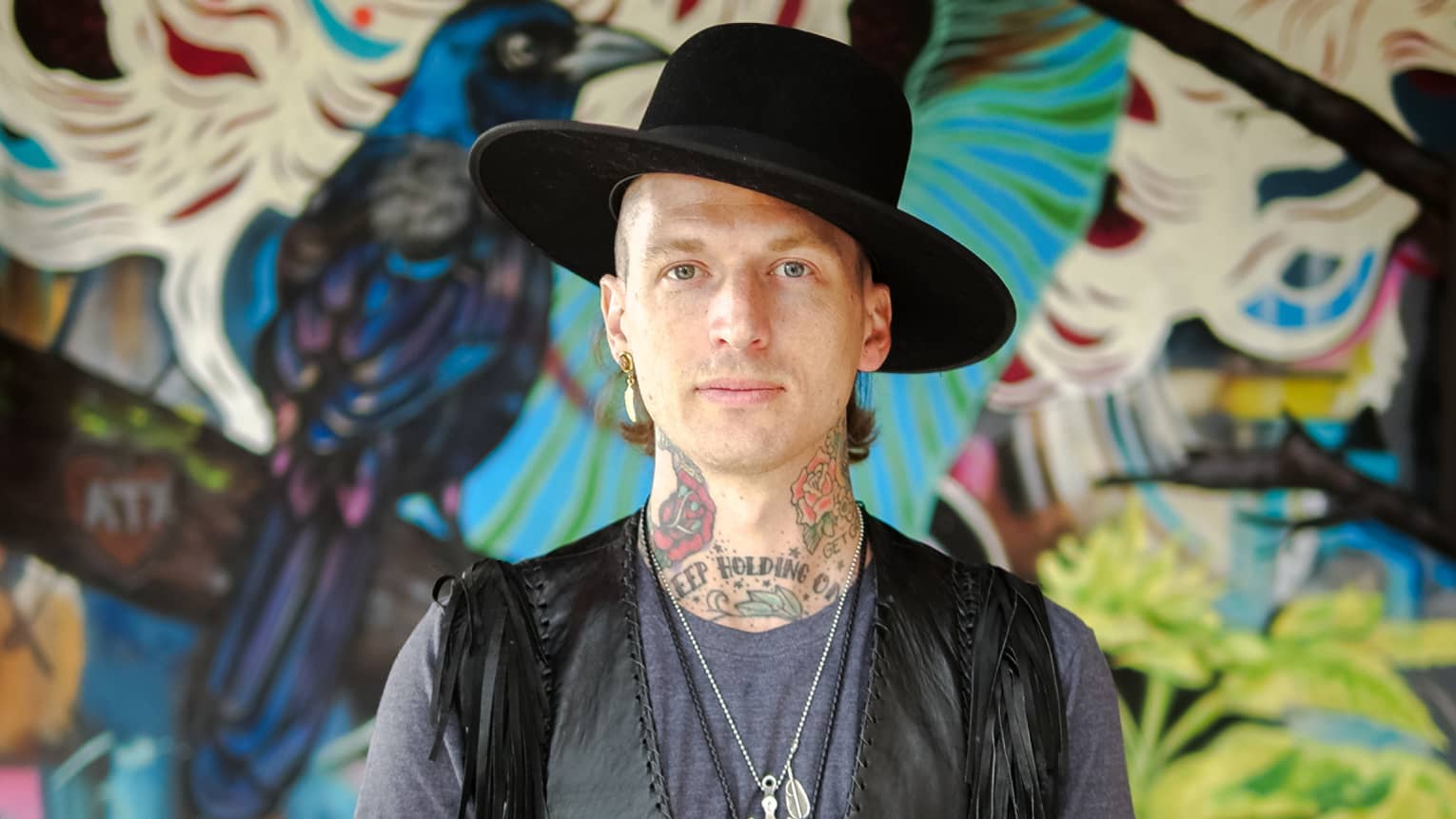 A portrait of Muralist Jason Eatherly in front of his mural on the patio at Ciclo.