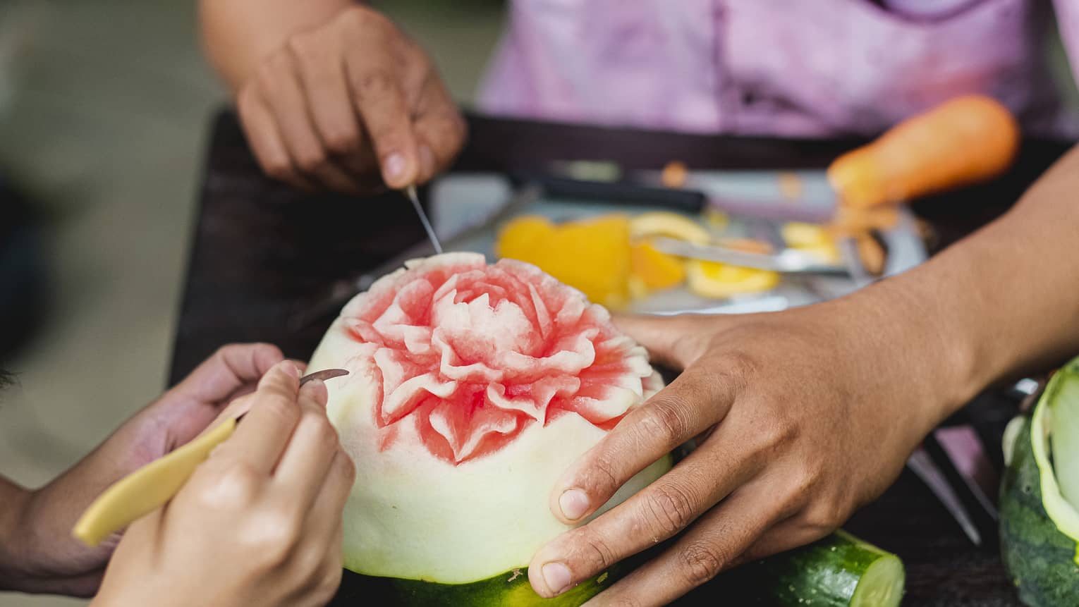 Close-up shot of man and child's hands carving intricate flower into watermelon