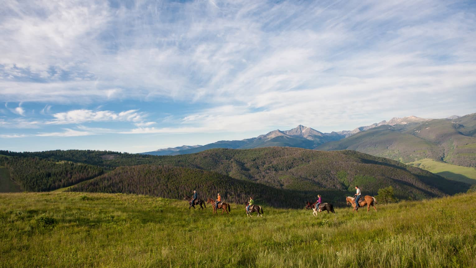 A group of people on horseback riding along grass and hills.