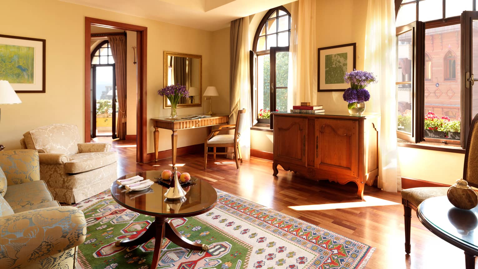Deluxe Suite bright living room with table over colourful kilim carpet, large windows