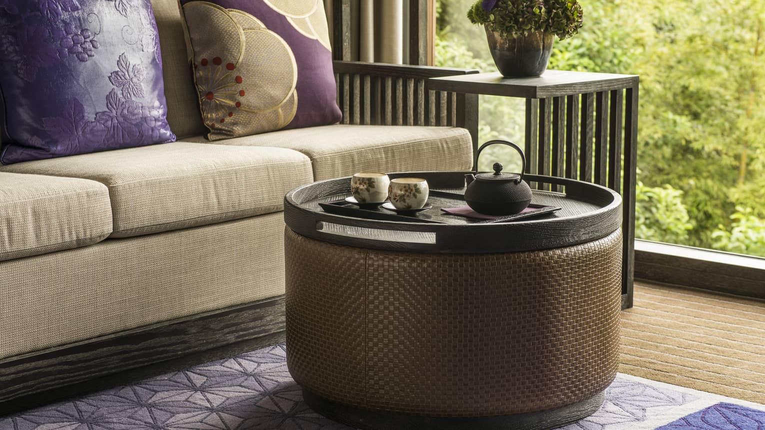 Close-up of beige sofa with purple pillows, round coffee table, garden view out window