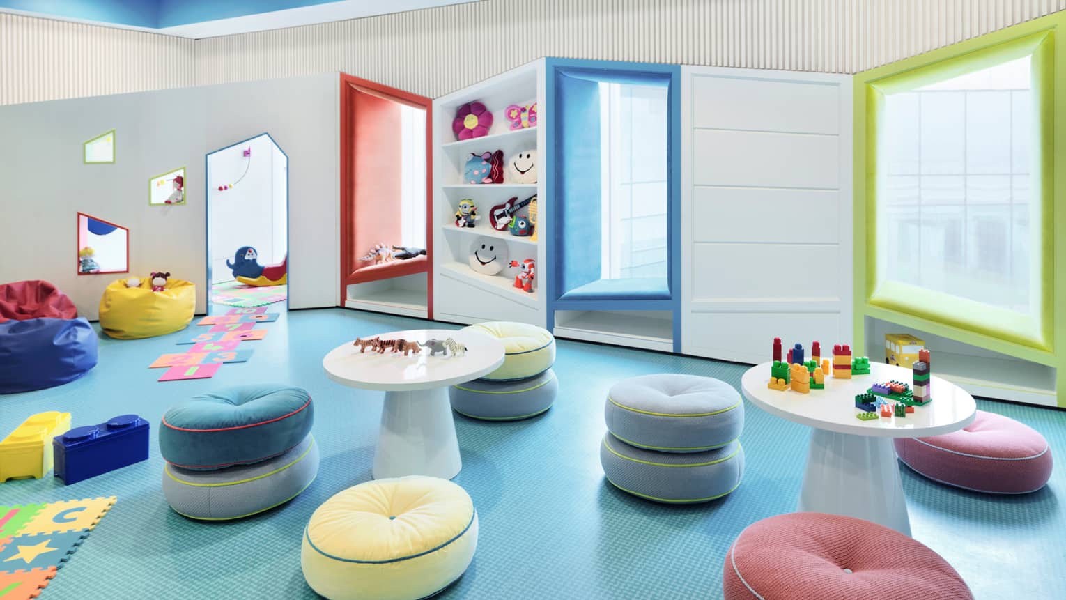 Kids for All Seasons play room with soft colourful stools, bean bag chairs, windows and shelf with toys