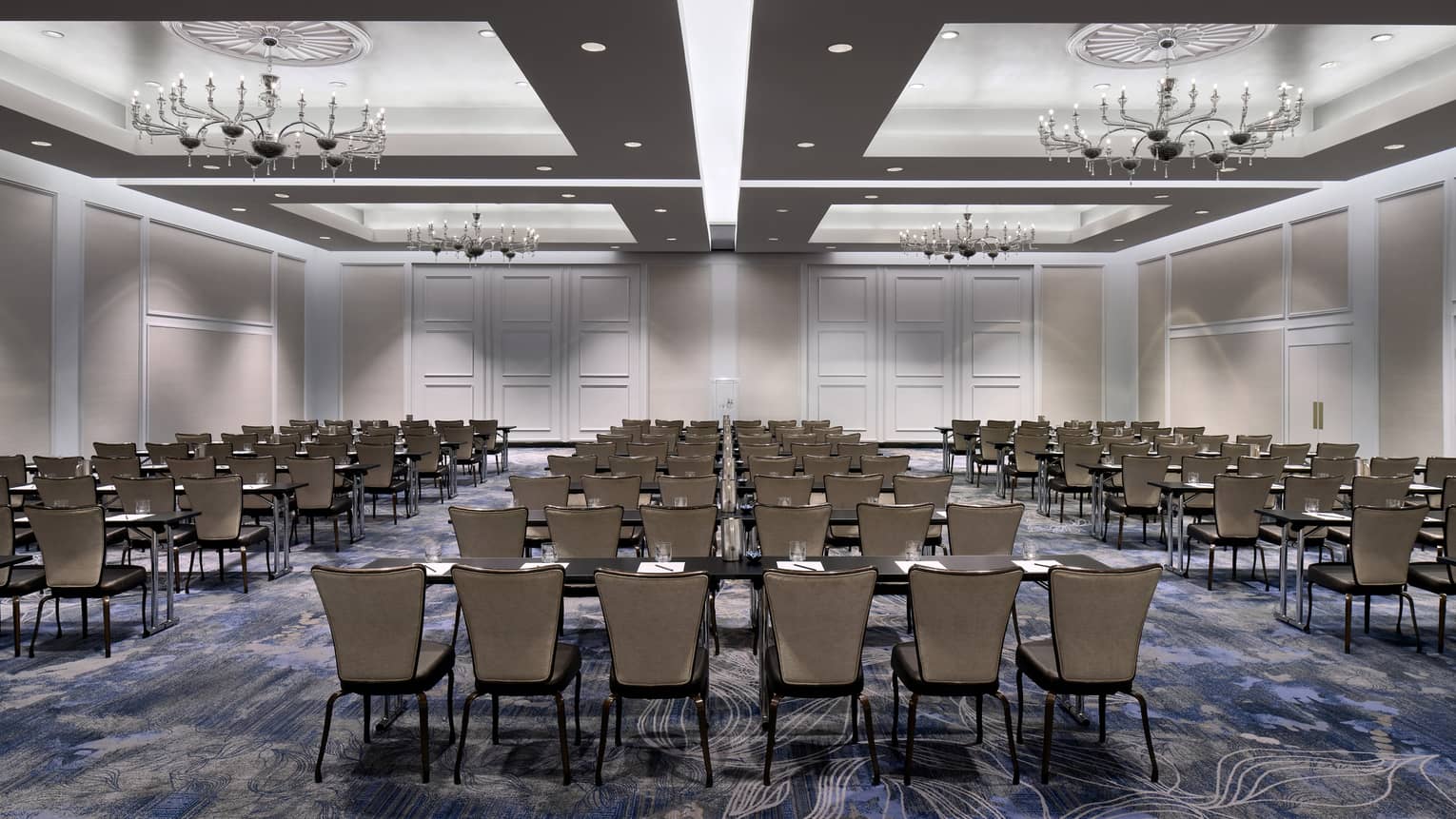 Large ballroom with inset ceilings, recessed lighting, and chandeliers, with several rows of tables and chairs