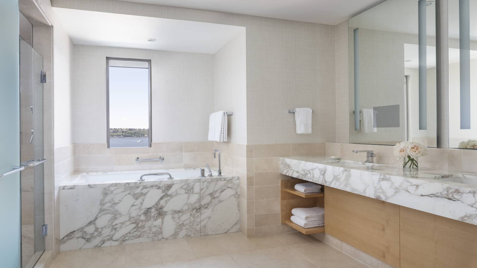 Marble countertops and a marble bathtub glow in the well-lit bathroom