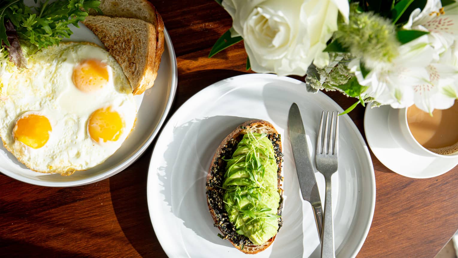Avocado toast, eggs, and coffee on a table near flowers.