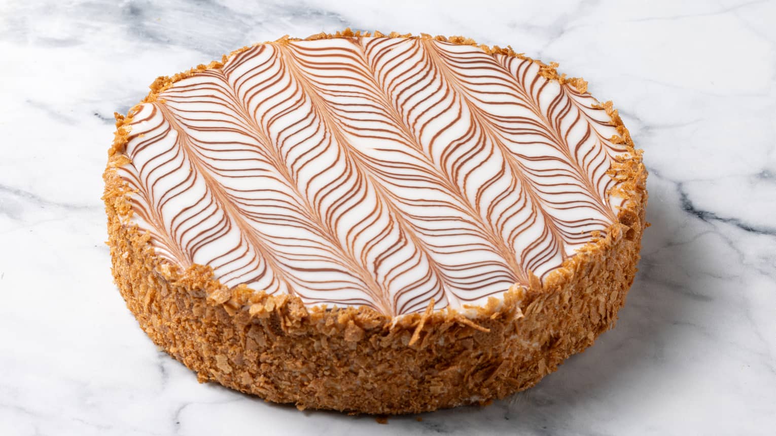 Round tan cake with crumble around sides and swirled top on marble surface
