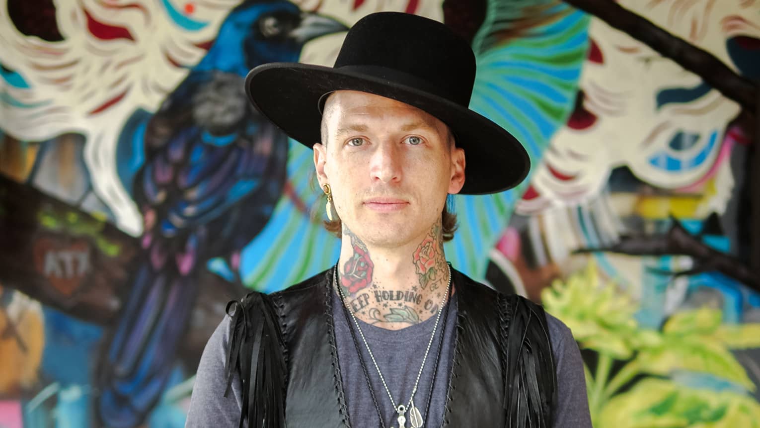 A portrait of Muralist Jason Eatherly in front of his mural on the patio at Ciclo.