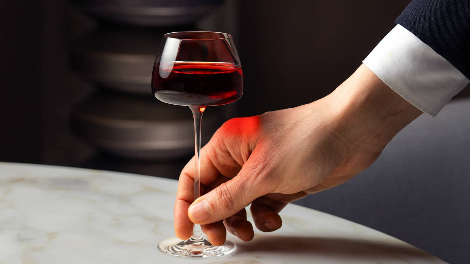 A hand sits down a glass of red wine on a white marble tabletop
