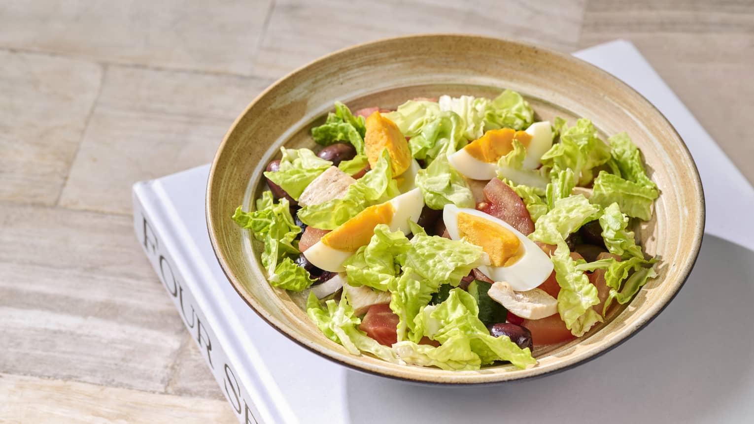 A salad with cooked eggs, tomato and bacon.