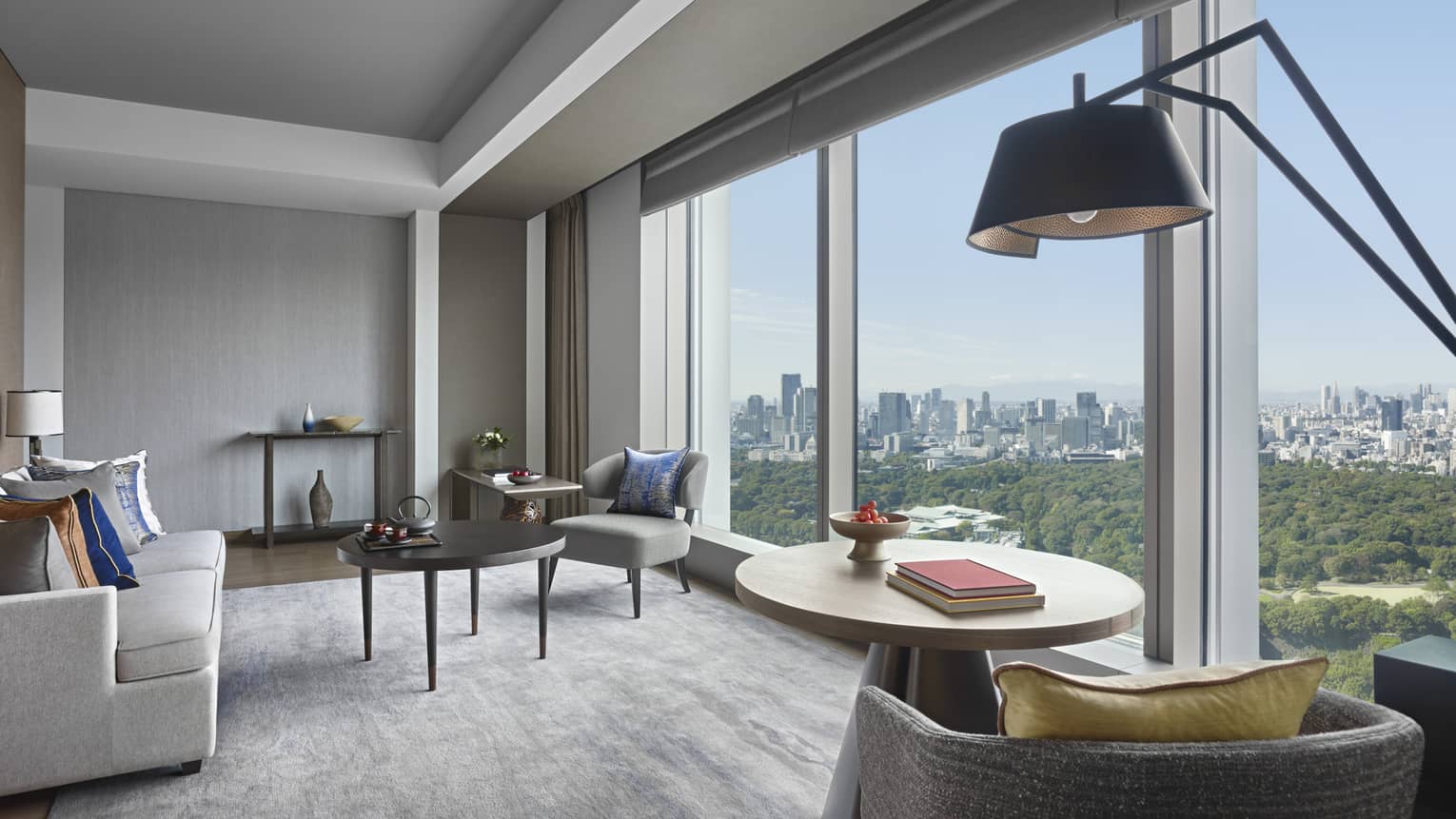 Bright hotel suite living room with floor to ceiling picture window overlooking trees, city