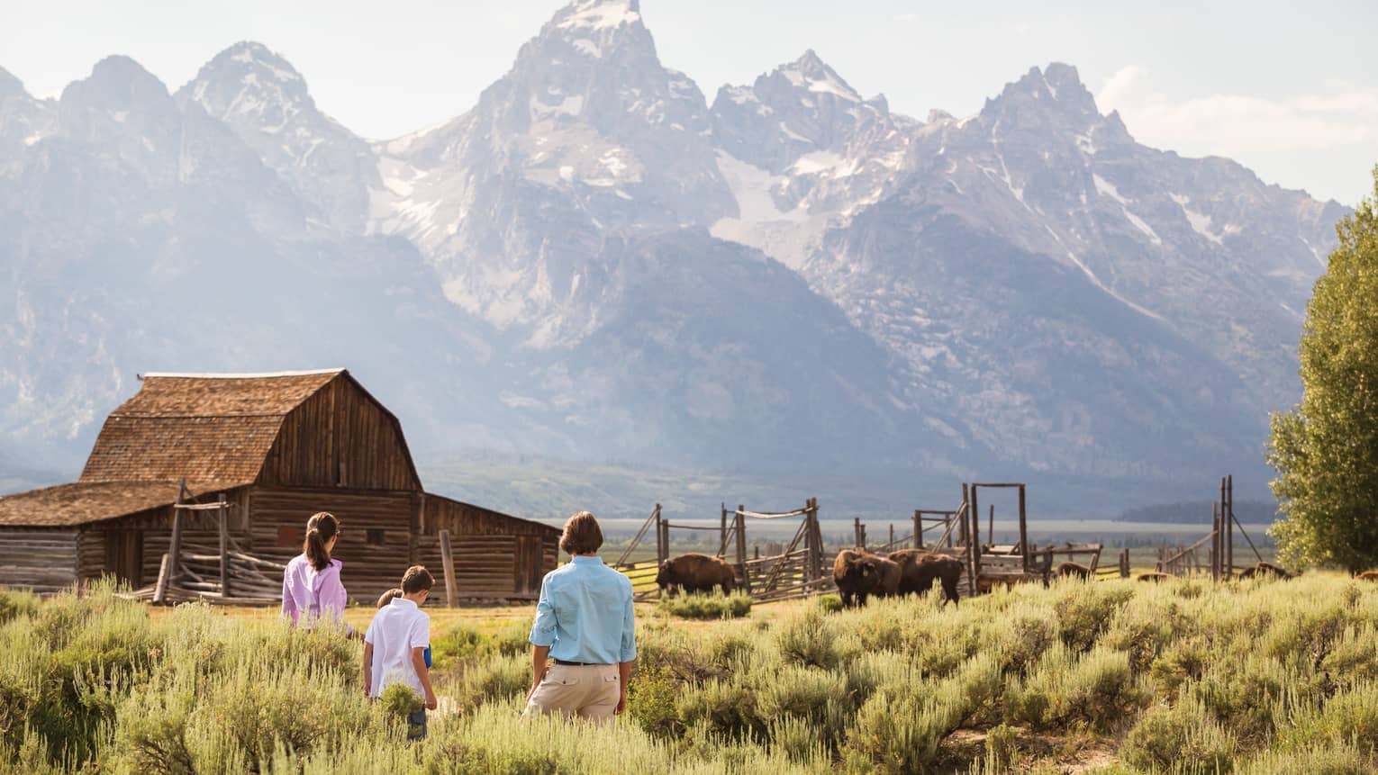 Family standing in a field with a cabin and mountains in the background.