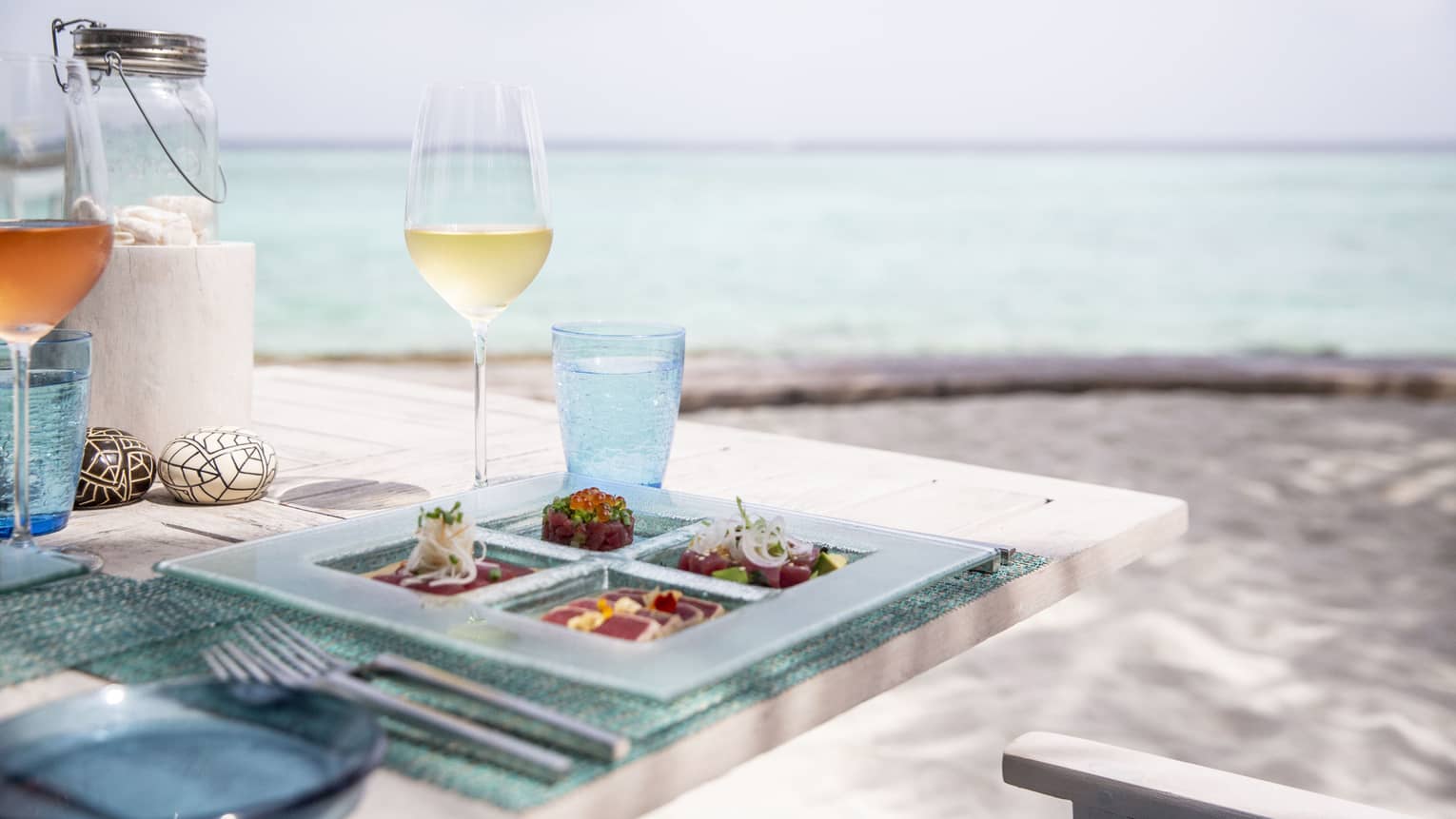 A tasetfully set table with a glass of white wine and rose overlooking the ocean at Fuego Grill