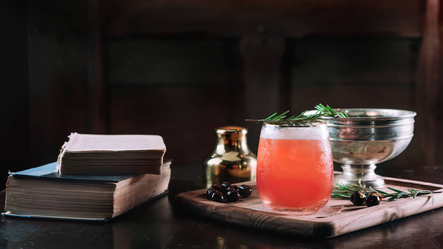 Red Biltmore Raspberry Smash cocktail with rosemary garnish on tray next to books
