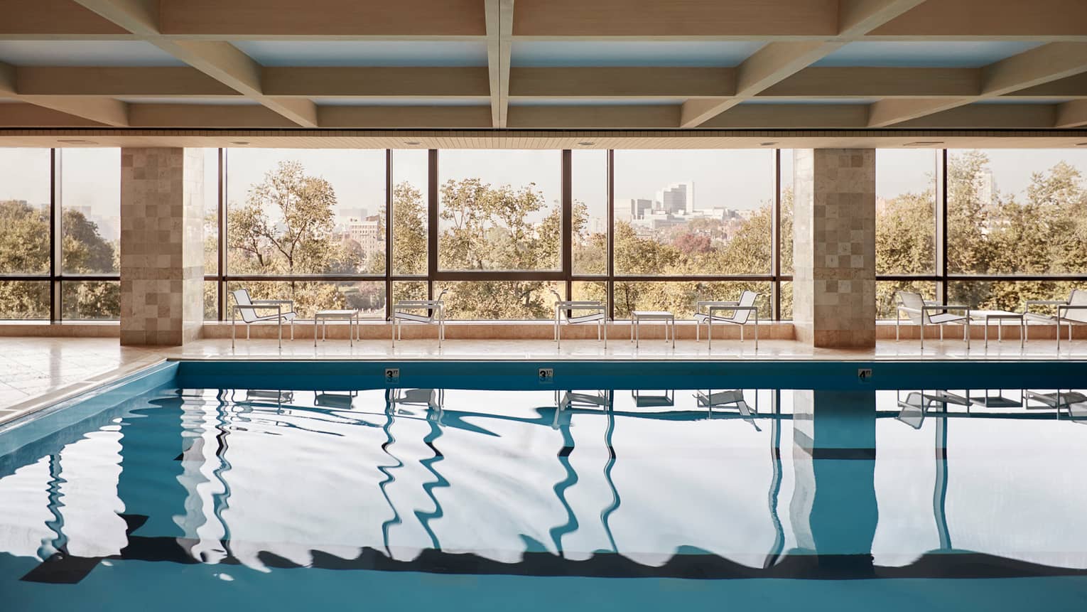 Reflection from sunny windows on calm blue indoor lap swimming pool with tables and chairs on deck