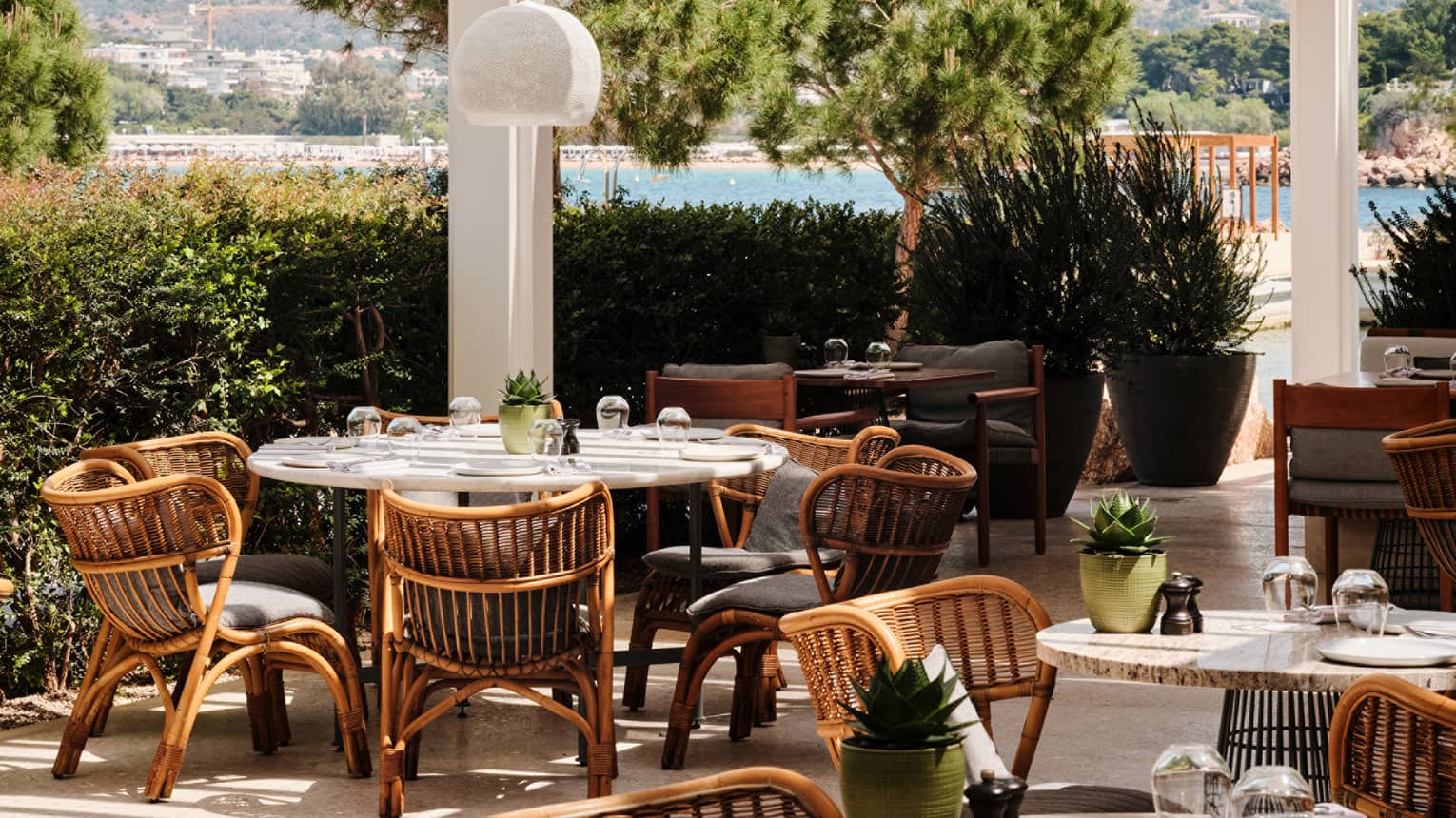 A spacious partly shaded outdoor dining area surrounded by greenery, with sea and coast views in the background