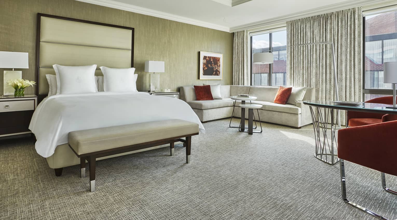 Grand Premier Room bed with white bench, tall padded headboard, L-shaped sofa near sunny picture window