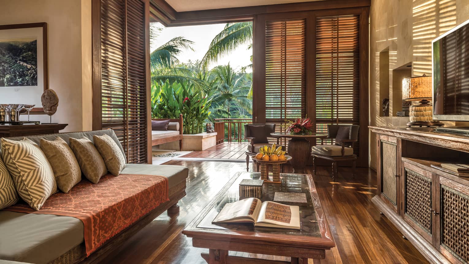 One-bedroom suite airy living room with hardwood floors, sofa and pillows, tables beside open wall to patio and garden