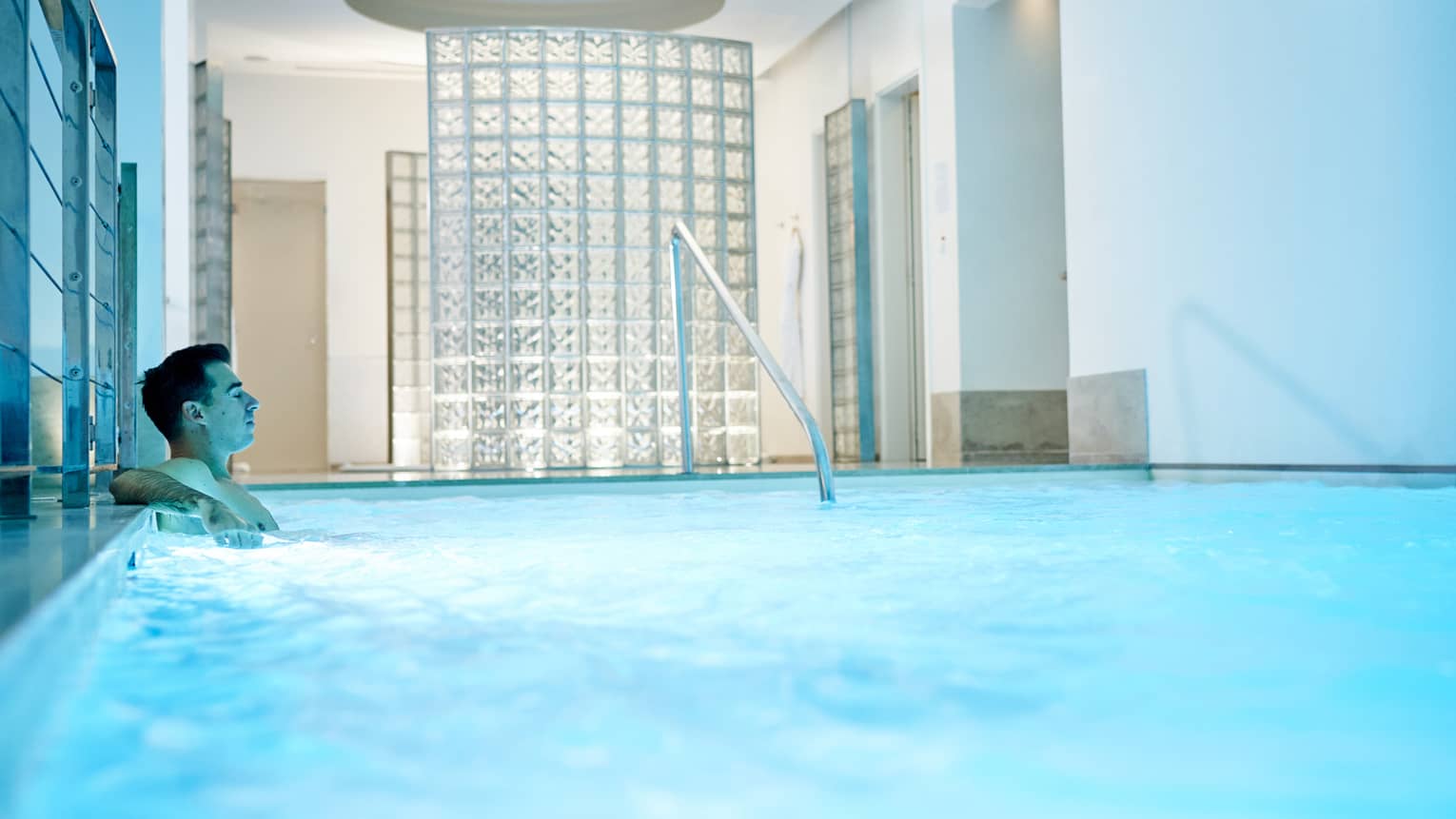 Man leans back in indoor pool with blue illuminated water