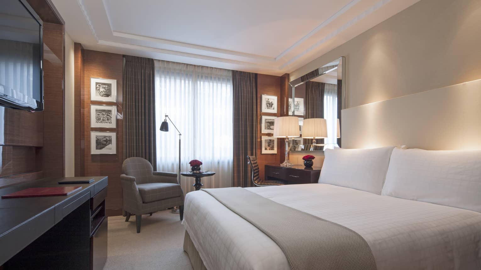 Superior Room bed with sash on white wall with accent lighting, armchair by curtains