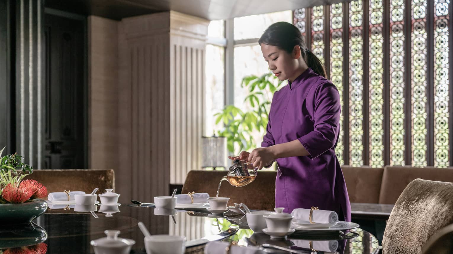 A person stands above a dining table pouring hot tea into a white mug