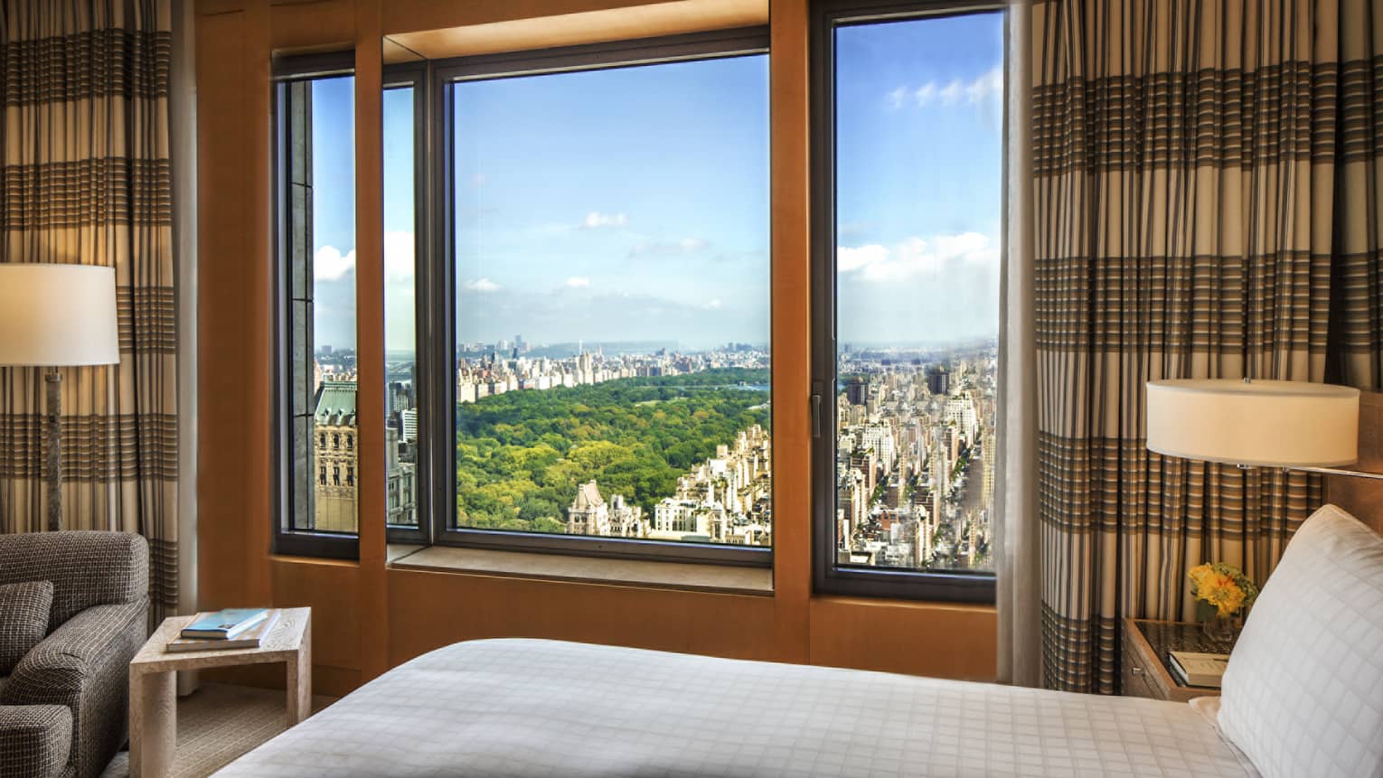 Central Park Suite bed and lamps by large window with striped curtains, park views 