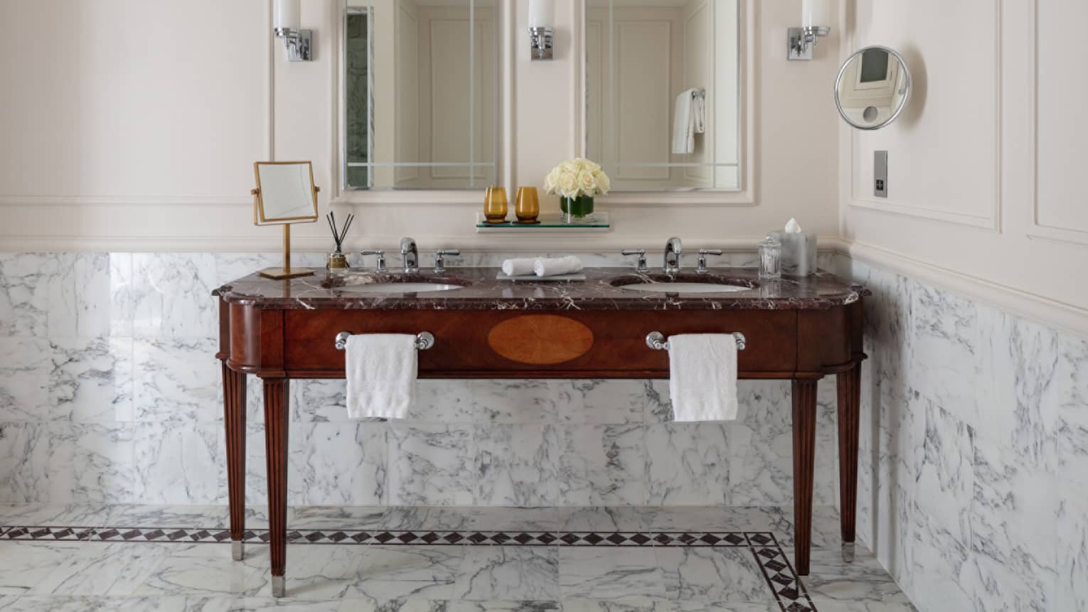 Bathroom with double wooden vanity, double mirror, marble tiles at chair rail, lighted wall sconces