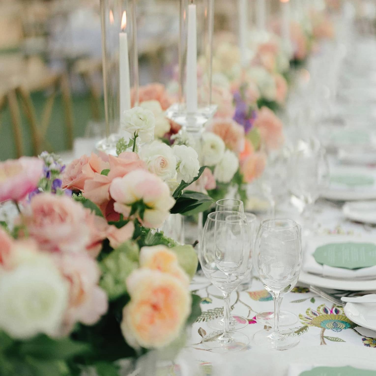 A banquet table lined with pink and white floral arrangements, glassware and candles