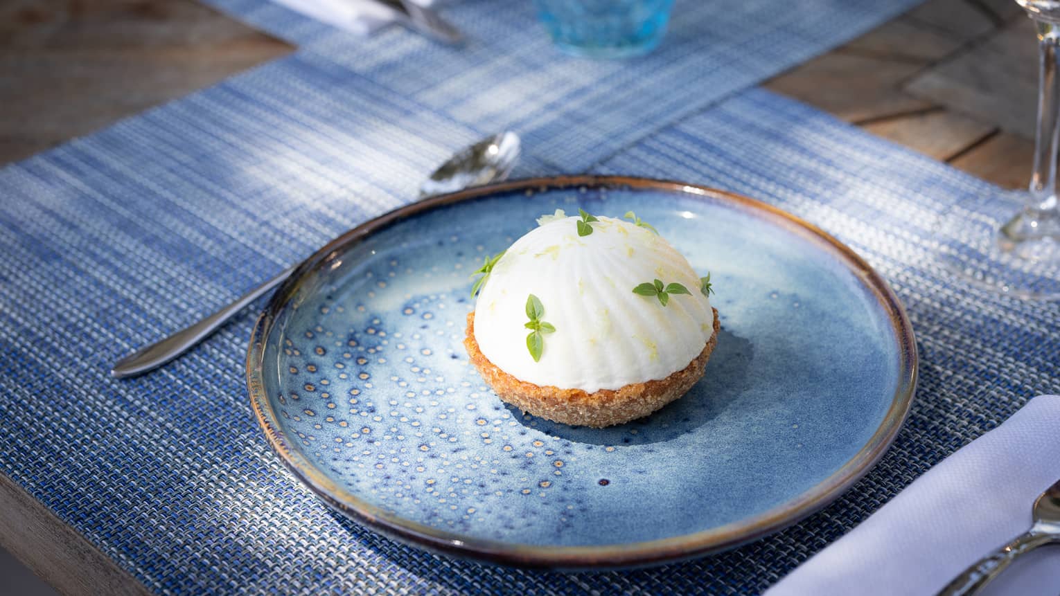 A white dome-shaped tart pastry topped with green leafy garnishes and served on a blue plate