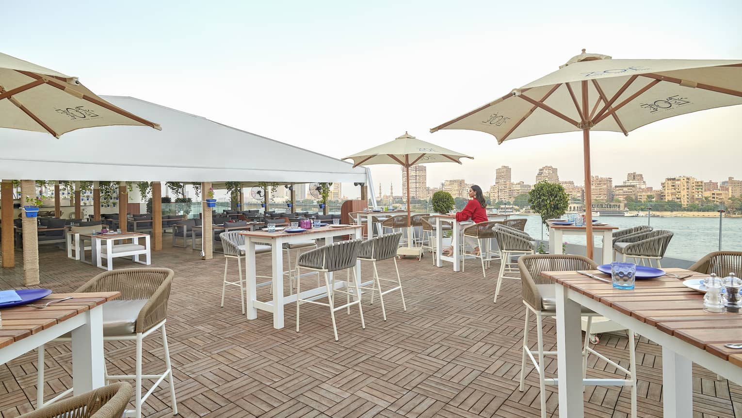 Woman in red dress seated at dining table on Zoe restaurant terrace over Nile views