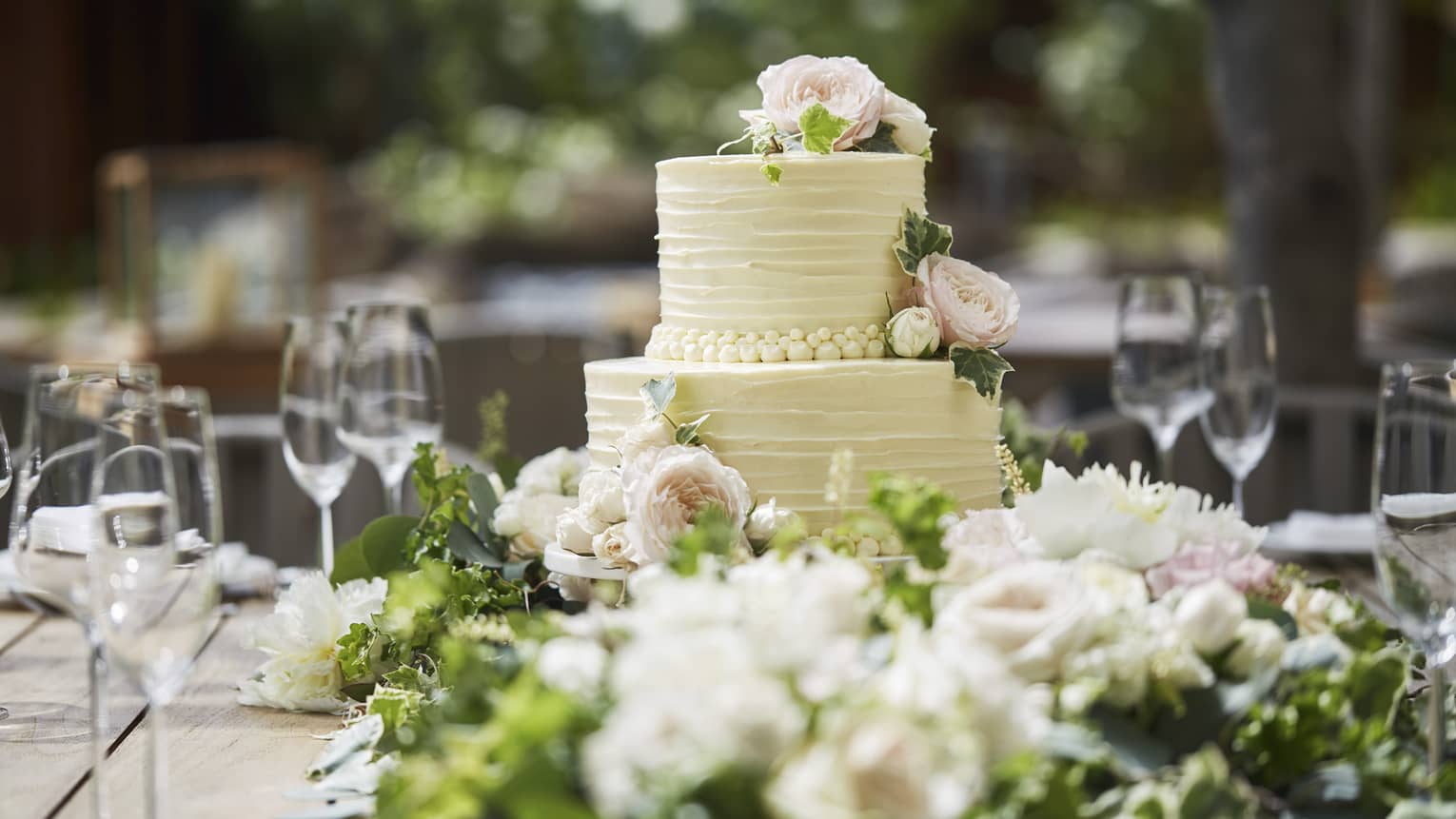 Two-tiered white wedding cake on banquet table with wine glasses, flowers