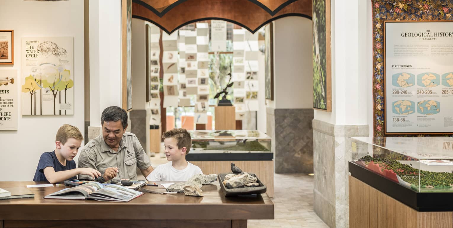 A man and two kids reading a book together at the Mangroves Discovery Centre at Four Seasons Langkawi